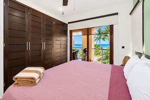 A bedroom with a large bed, a balcony with a view of the ocean, and a sliding door leading to the balcony.