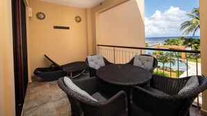 Een balkon met rieten meubilair, uitzicht op zee en een palmboom.