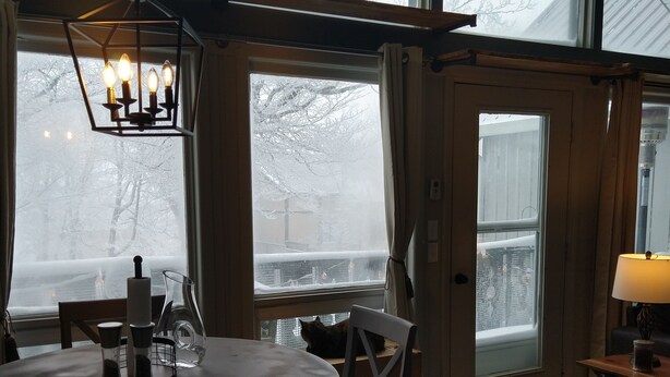 A cozy room with a round wooden table, chairs, a hanging light fixture, and large windows with frosty views. - Welcome to the stunning Bergbewohner ski chalet! (Beech Mountain)