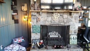 A cozy room with a stone fireplace, a television mounted above it, and a comfortable seating area with a bean bag and pillows. - Welcome to the stunning Bergbewohner ski chalet! (Beech Mountain)