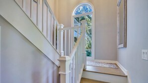 A staircase with white railings and wooden steps leading to a landing with a large arched window.