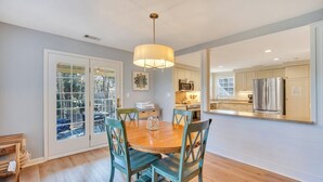 A dining area with a wooden table and chairs, a pendant light, and a view into the kitchen.