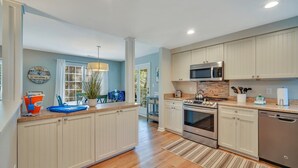 A modern kitchen with light wood cabinets, stainless steel appliances, and a large island with seating.