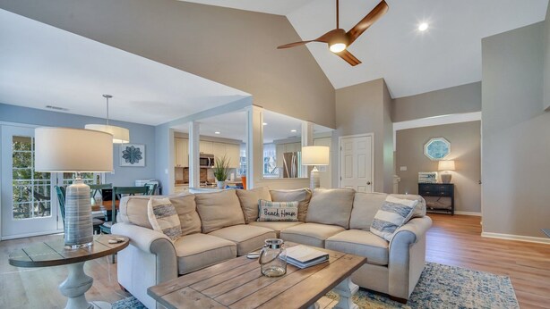 A spacious living room with a large beige sectional sofa, a wooden coffee table, and a ceiling fan.