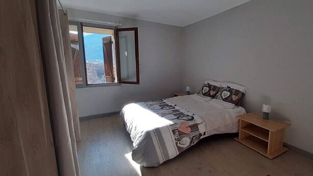 Une chambre à coucher avec un lit, une table de chevet, une fenêtre avec des rideaux et une vue sur le paysage urbain.
