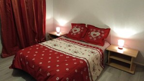 Une chambre à coucher avec un lit, des rideaux rouges, deux tables de chevet avec des lampes et une couvre-lit à motifs rouges et blancs.