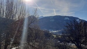 Un paysage montagneux avec un ciel dégagé, des arbres au premier plan et une vue lointaine d’une ville ou d’un village.