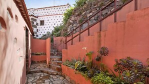 Un estrecho callejón empedrado con una escalera que sube hacia un edificio de fachada blanca y pared roja.
