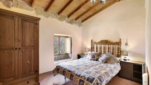Un dormitorio con un armario de madera, una cama con cubrecama estampado, una mesita de noche y una ventana con vistas a árboles.