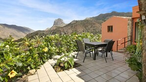 Un patio con mesa y sillas, rodeado de abundante vegetación y vistas a la montaña.