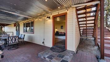 A covered patio area with outdoor seating, a wooden staircase, and a view of the interior.