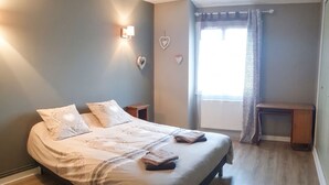 Une chambre à coucher avec un lit, des tables de chevet, une lampe fixée au mur, une fenêtre avec des rideaux et un objet décoratif en forme de cœur.