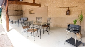 Une terrasse extérieure avec une table et des chaises, un barbecue et un mur en pierre.
