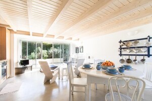 Cocina moderna con comedor, que presenta techo de madera, ventanas amplias y un colgador de ollas en la pared.