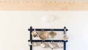 Een eetruimte met een ronde tafel, gedekt met blauw servies en een schaal fruit. Een wandrek bevat diverse keukengerei.