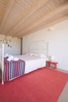 Un dormitorio con cama blanca, alfombra roja y techo de madera.