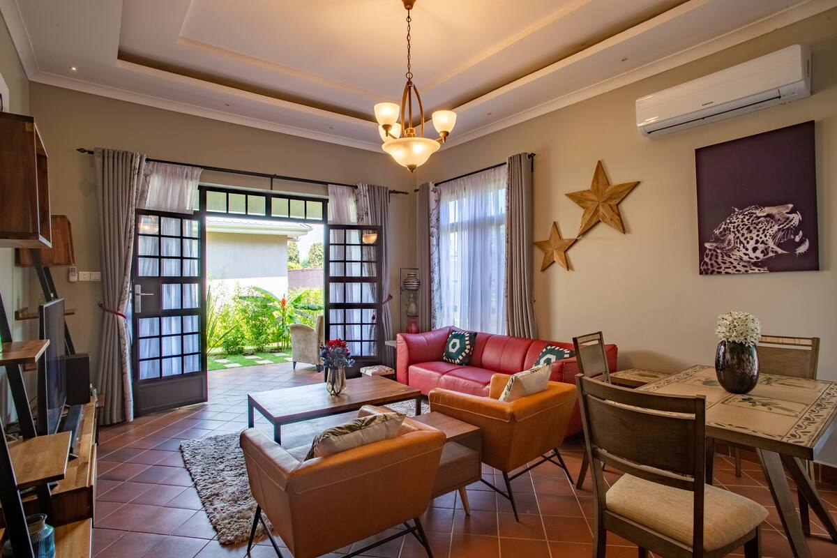 A spacious living area with a red leather sofa, wooden chairs, a coffee table, and a dining table with a vase of flowers.
