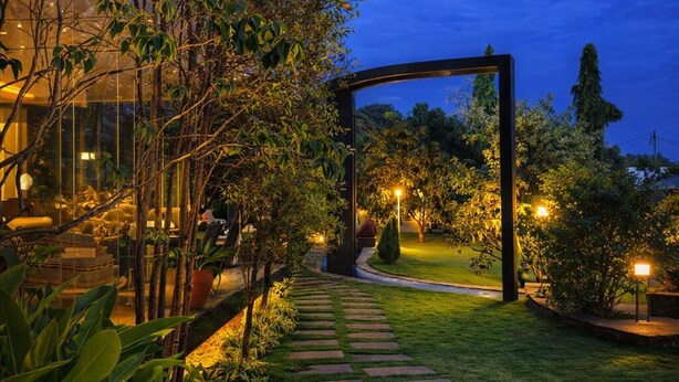 Un sendero de jardín que lleva a una estructura con fachada de vidrio, rodeada de follaje y con iluminación ambiental.