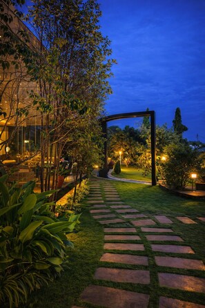 A garden pathway leading to a structure with a glass facade, surrounded by greenery and illuminated by ambient lighting. - Kinga Home Suites (Moshi)