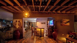 Un rincón de bar acogedor con suelo de madera, barra y asientos. Hay jarrones grandes y una lámpara con forma de globo.