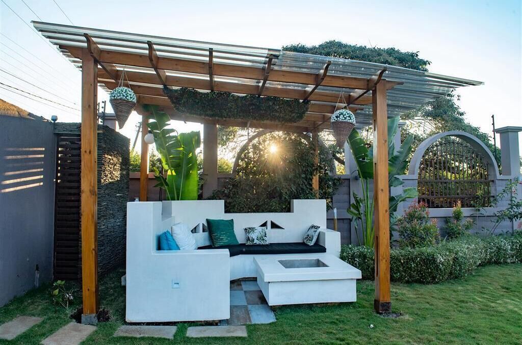Un espace extérieur moderne, aménagé avec un canapé blanc, une pergola et une végétation luxuriante.