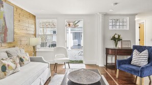 Ein Wohnzimmer mit einem weißen Sofa, einem blauen Sessel, einer Holzwand und Blick ins Freie.