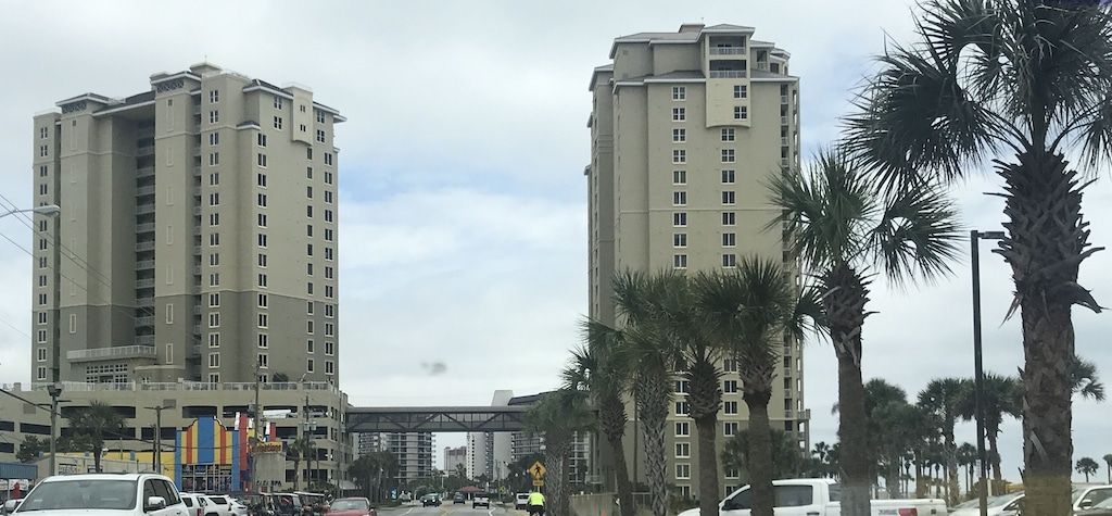 A multi-story building with a flat facade, surrounded by palm trees and a busy street with cars.