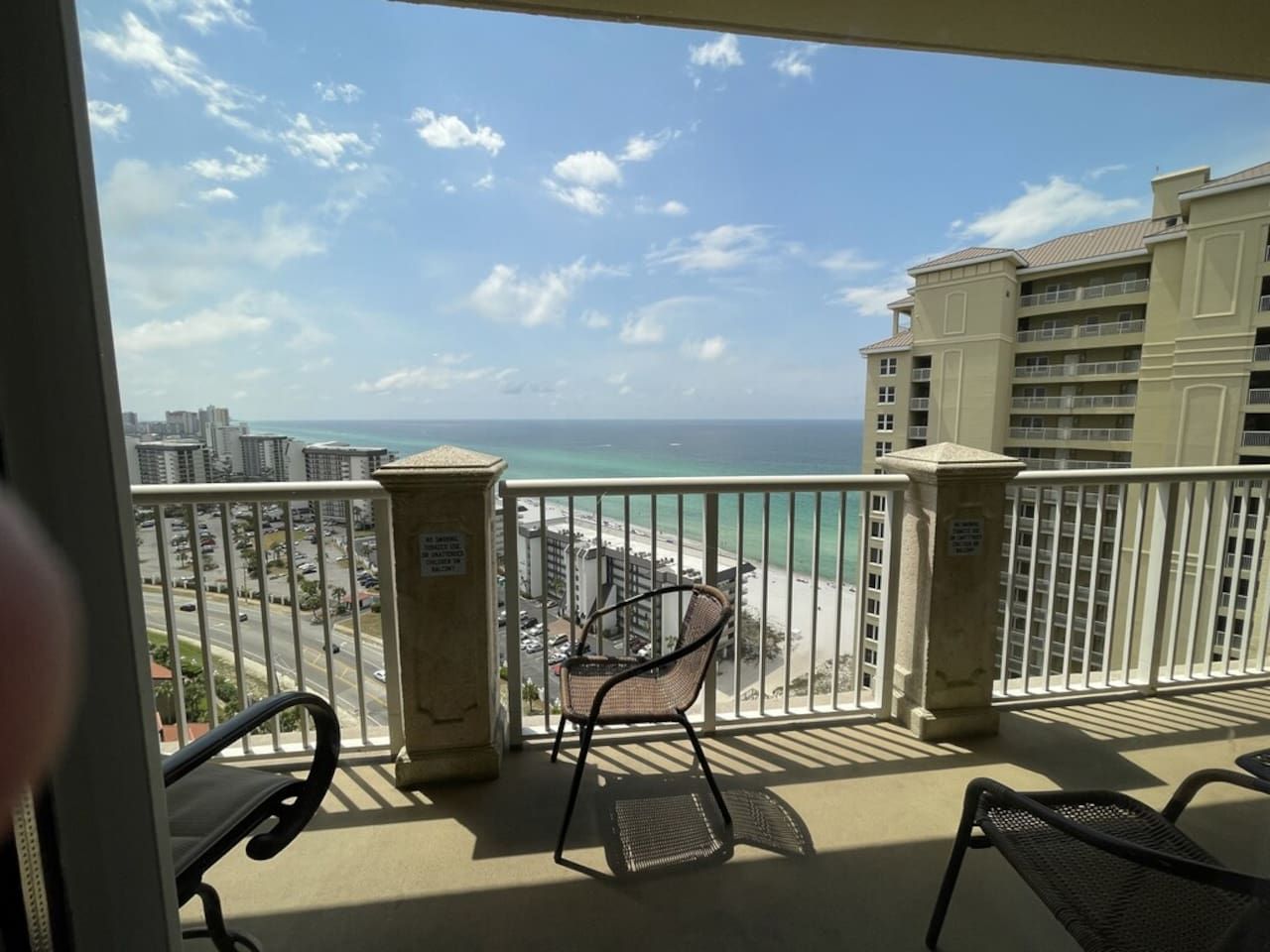 A balcony with a view of the beach and ocean, featuring a chair and a table.