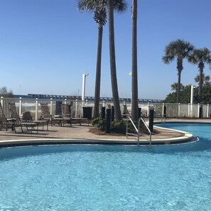 Ein Swimmingpool mit Holzterrasse, Palmen und einem Zaun.