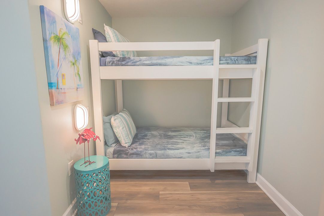 A bunk bed with a view of the sky through a window, a small round table with a decorative item, and a painting on the wall.