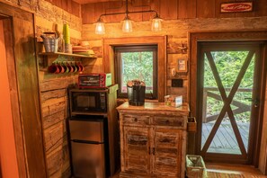 Compact kitchen with a refrigerator, microwave, and coffee maker, offering a view of the surrounding greenery.