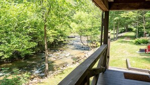 A wooden deck overlooking a stream with surrounding greenery.