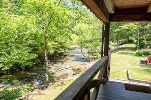 Relax on the deck overlooking a serene natural landscape with a flowing stream and lush trees.