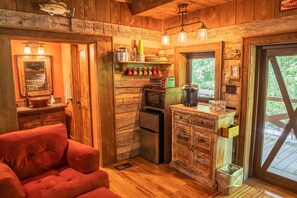 Relax in this cabin-style room with a compact kitchen, wooden walls, and a large window offering a forest view.