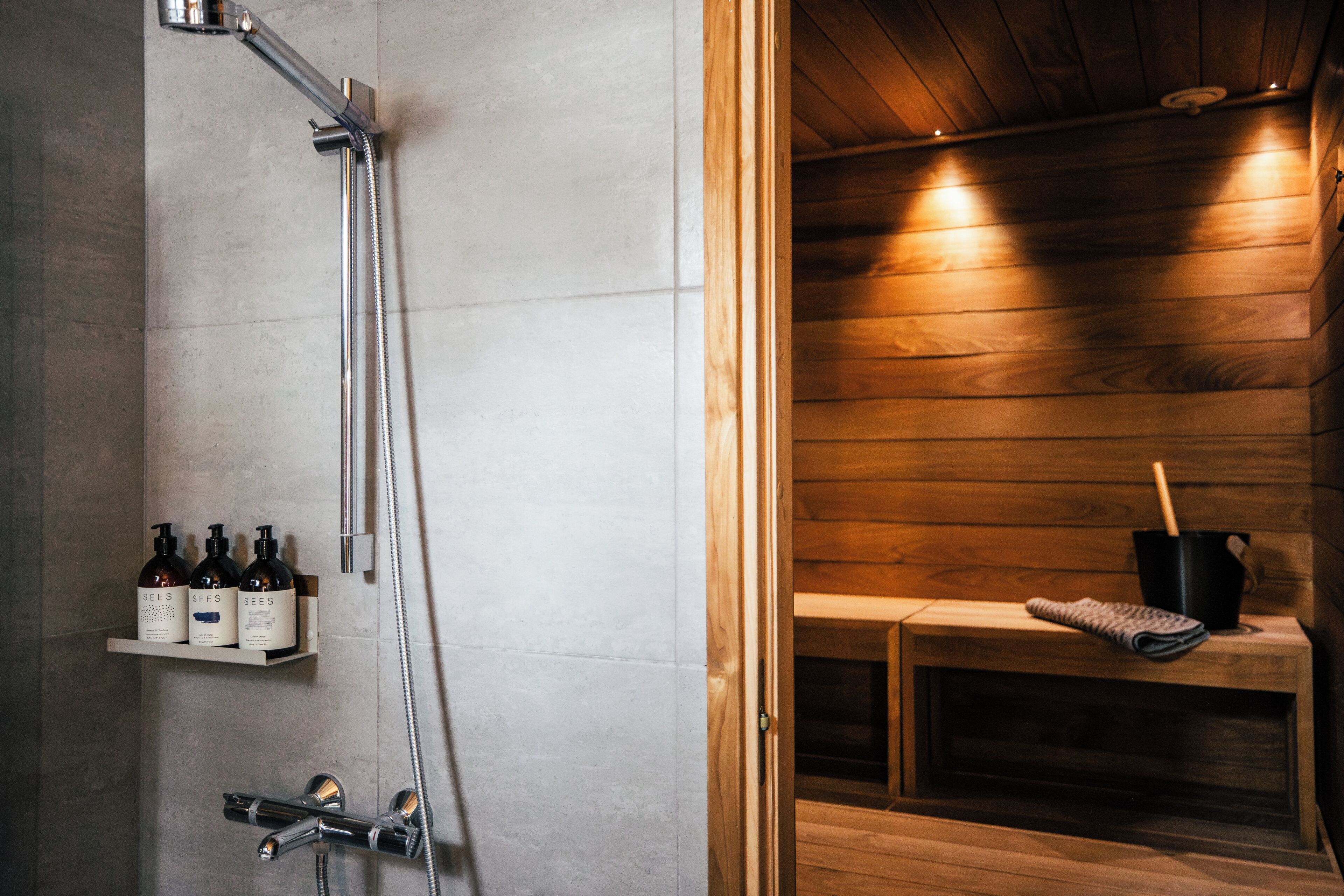 Un baño moderno con ducha, un banco de madera y un estante con botellas.