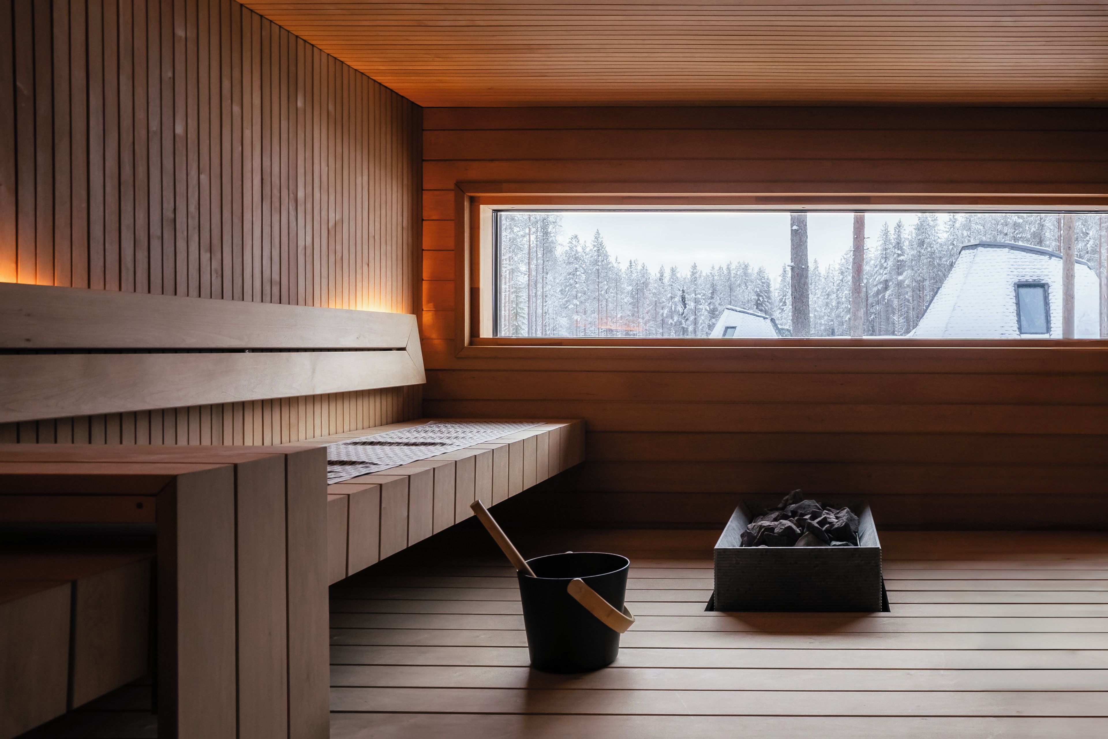 A wooden interior with a bench, a window, and a black bucket.