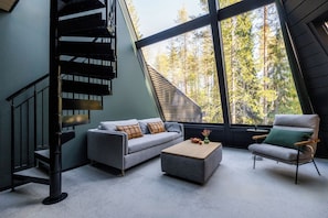 A modern interior with a grey sofa, a wooden coffee table, and a green armchair. A spiral staircase leads to an upper level.