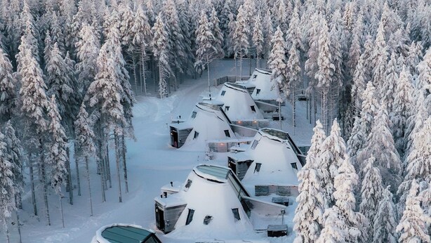 A row of snow-covered yurts in a forest, each with a sloped roof and a small porch area. - Glass Resort (Rovaniemi)