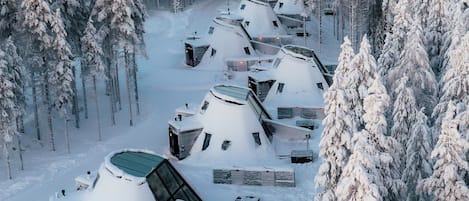 Une rangée de yourtes enneigées dans une forêt, chacune ayant un toit en pente et un petit espace de véranda.
