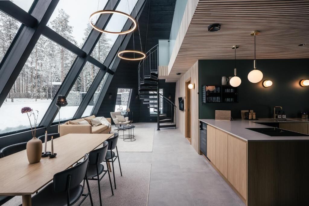 A modern interior with a dining area, kitchen, and large windows overlooking a snowy landscape.