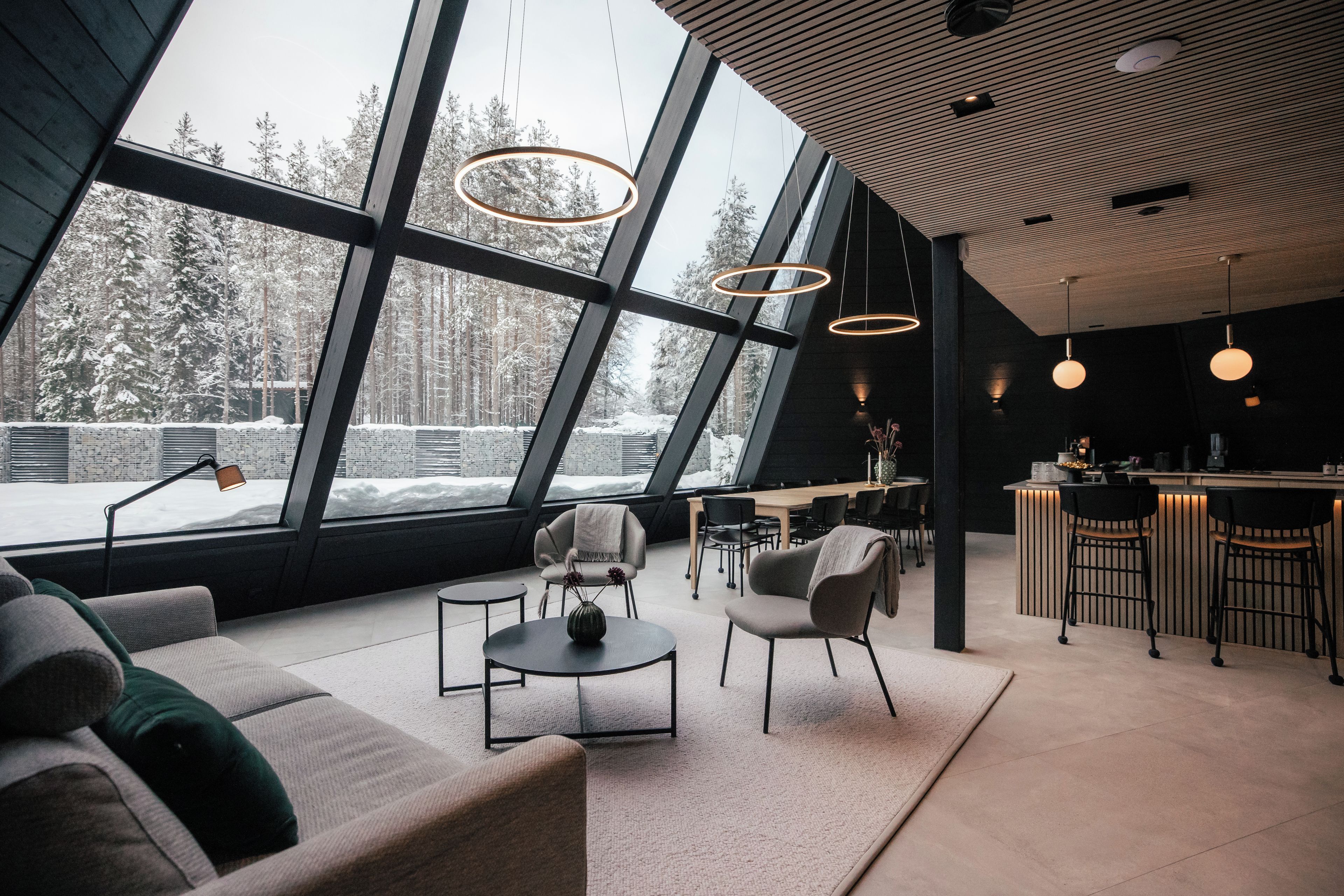 A modern interior with a large window offering a snowy forest view, a cozy seating area, and a bar.