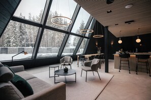 A modern interior with a large window offering a snowy forest view, a cozy seating area, and a bar. - Glass Resort (Rovaniemi)