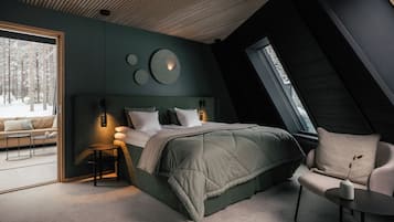 A modern bedroom with a large bed, a seating area, and a view of a snowy forest.