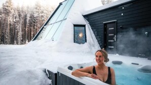 A person in a hot tub outside a building with a sloped roof, surrounded by snow. - Glass Resort (Rovaniemi)