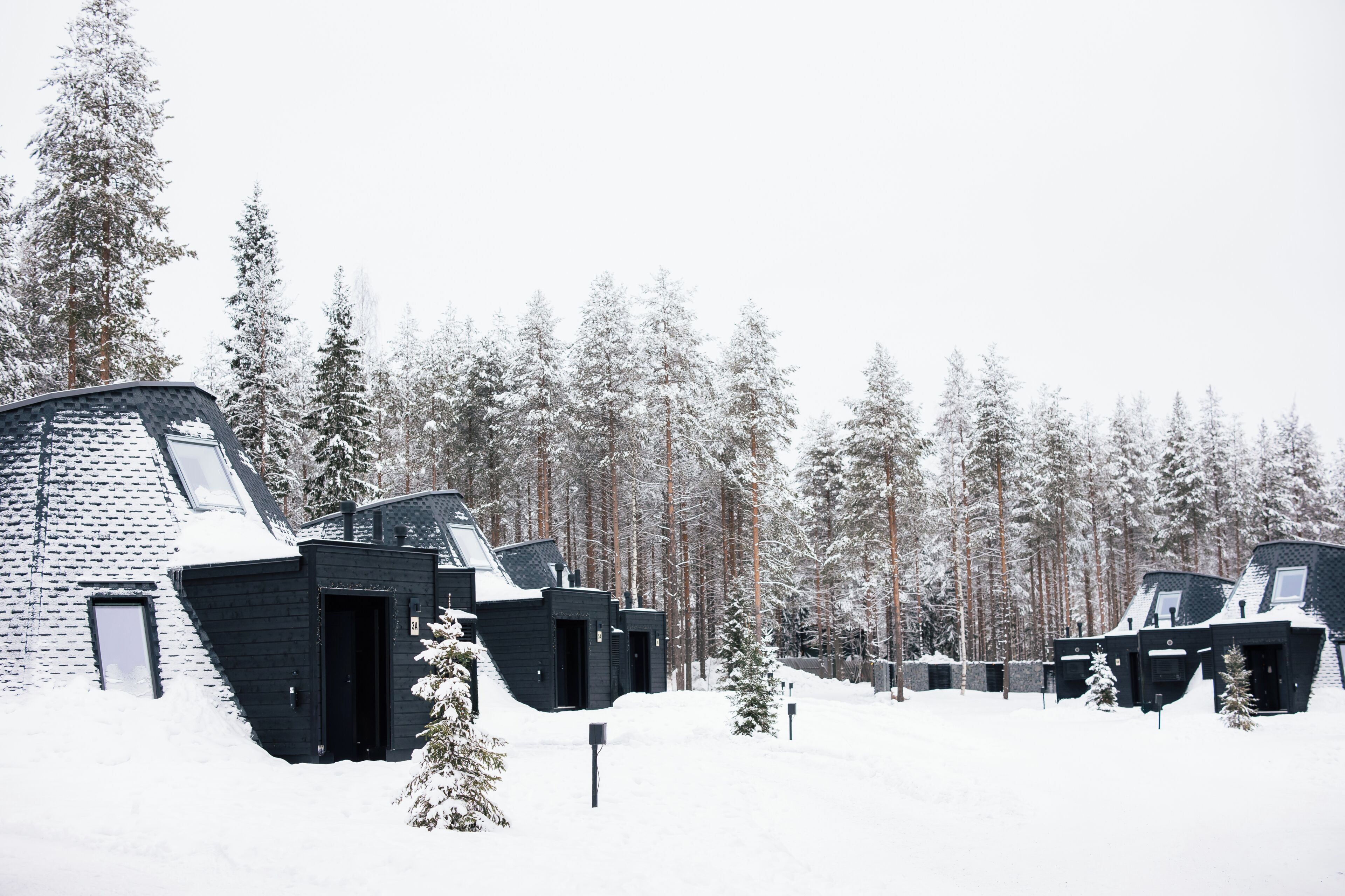 A row of cabins with a sloped roof, surrounded by a snowy forest.