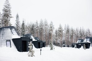 A row of cabins with a sloped roof, surrounded by a snowy forest.