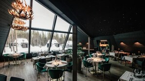 A restaurant with round tables and chairs, large windows, and a modern chandelier. - Glass Resort (Rovaniemi)