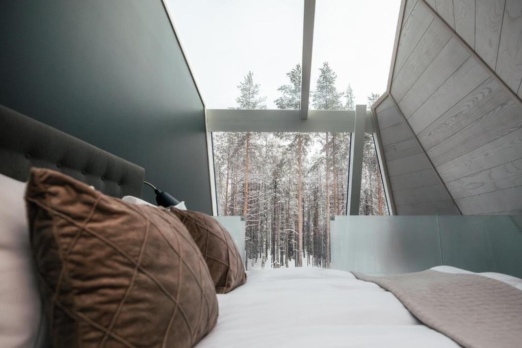 Un dormitorio con cama, almohadas y vista a un bosque a través de una ventana.