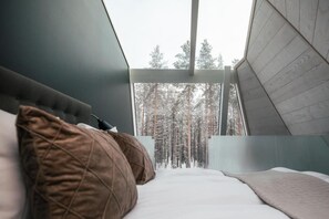 A bedroom with a bed, pillows, and a view of a forest through a window.