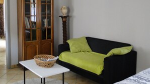 Een kamer met een zwarte bank, een witte tafel met een mand, een houten kast en een bed met een decoratieve spreideken.